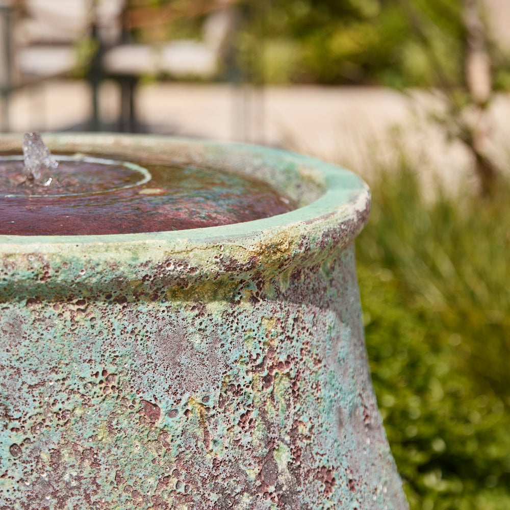Rustic stone effect water feature with a blurred garden background