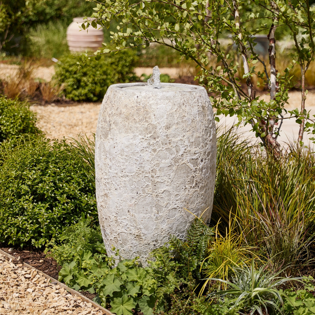 Decorative stone vase water feature in a garden setting with greenery