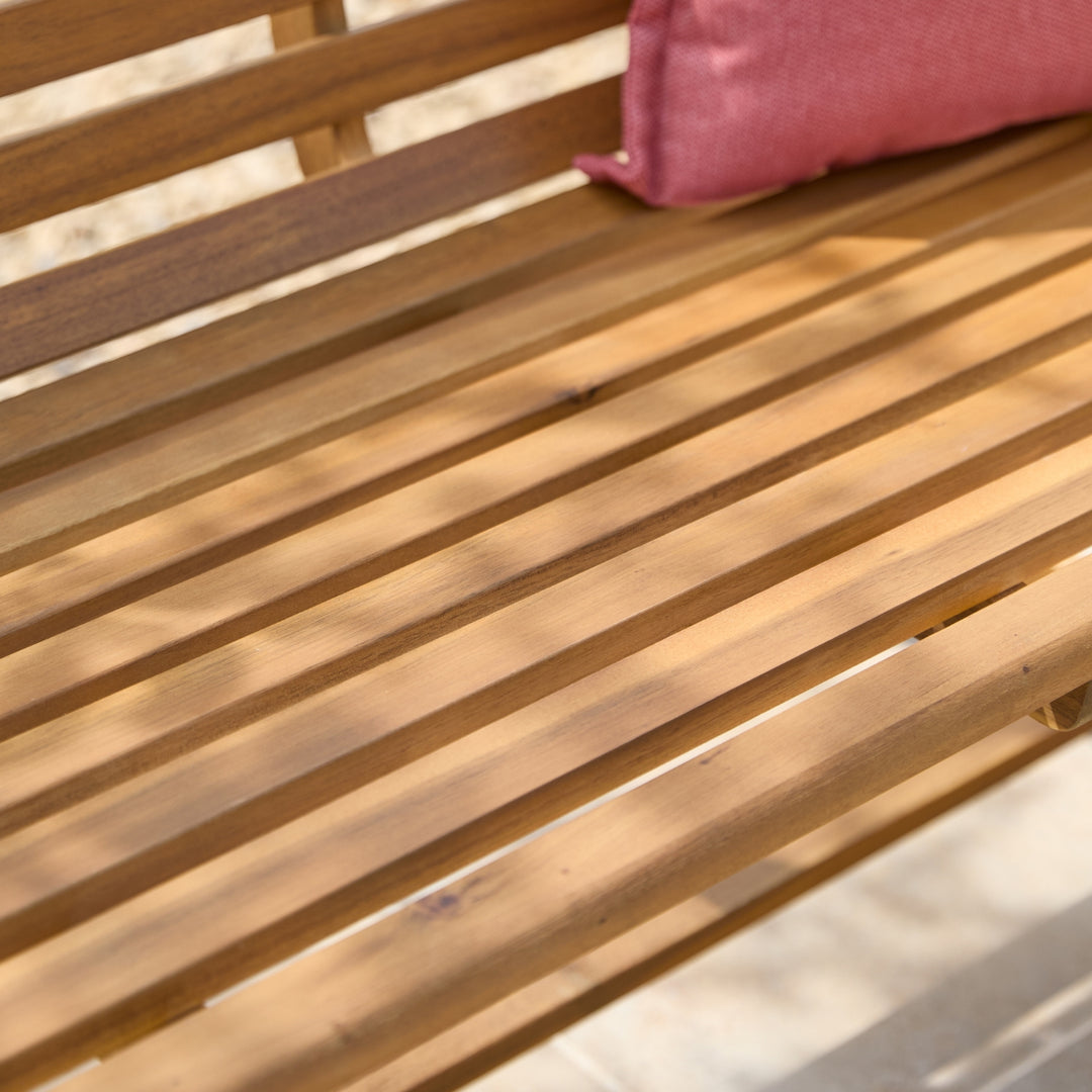 Close-up of a wooden slatted bench or chair with a pink cushion resting on the seat.