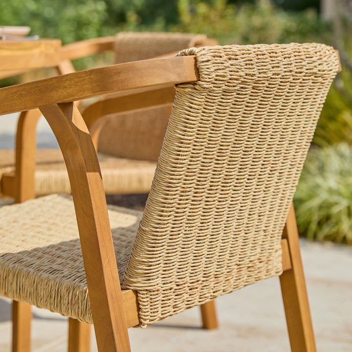 Outdoor patio dining chair with a natural woven rope seat and backrest and a light brown acacia wooden frame, shown in a garden setting.
