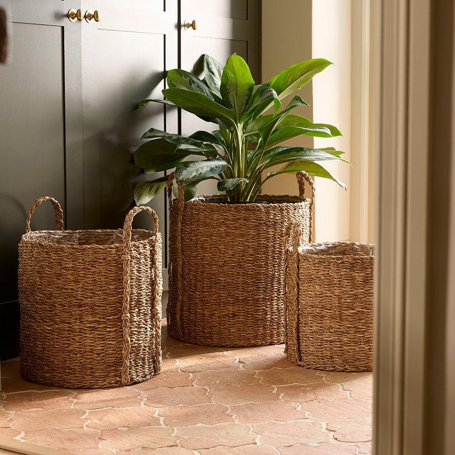 Three woven baskets with a plant on a stone floor