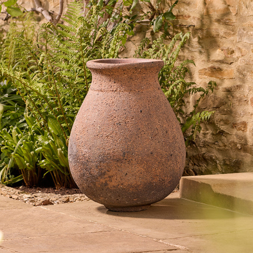 Rustic clay pot on a stone patio with greenery and a stone wall in the background
