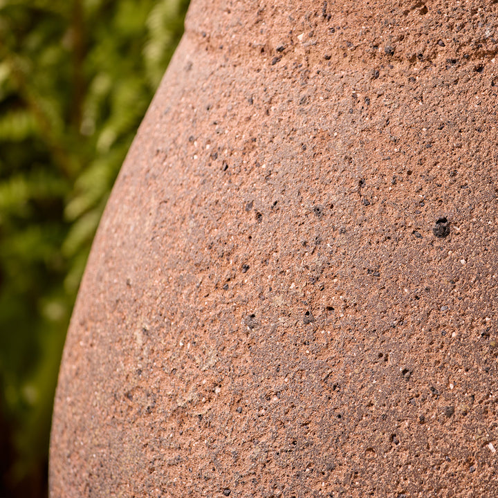 Close-up of a textured brown stone plant pot finish with a blurred green garden background