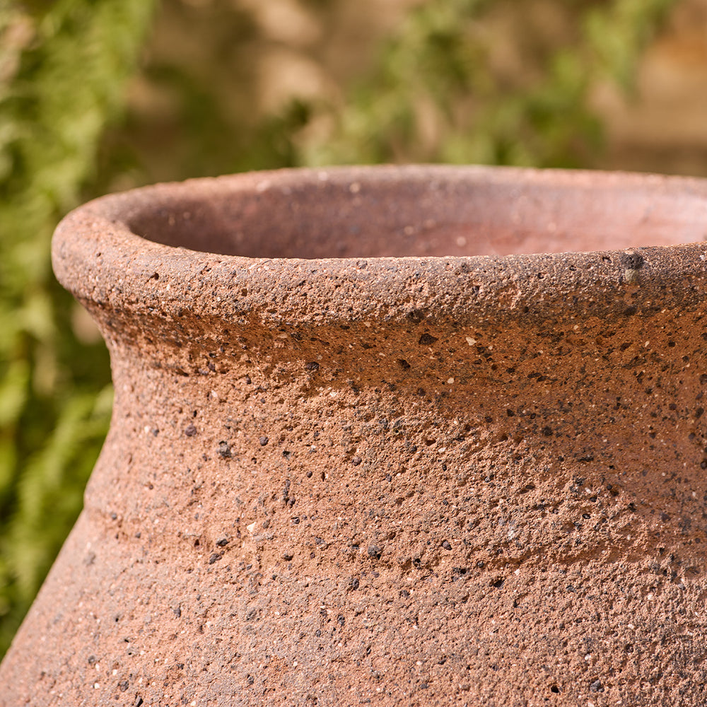 Close-up of a terracotta old stone pot with a blurred green background