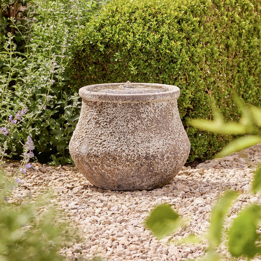 Decorative stone water feature on a gravel surface with greenery in the background