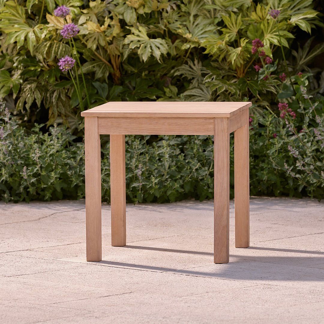 Natural finish wooden garden furniture table with clean lines and compact design, set on a stone outdoor terrace.