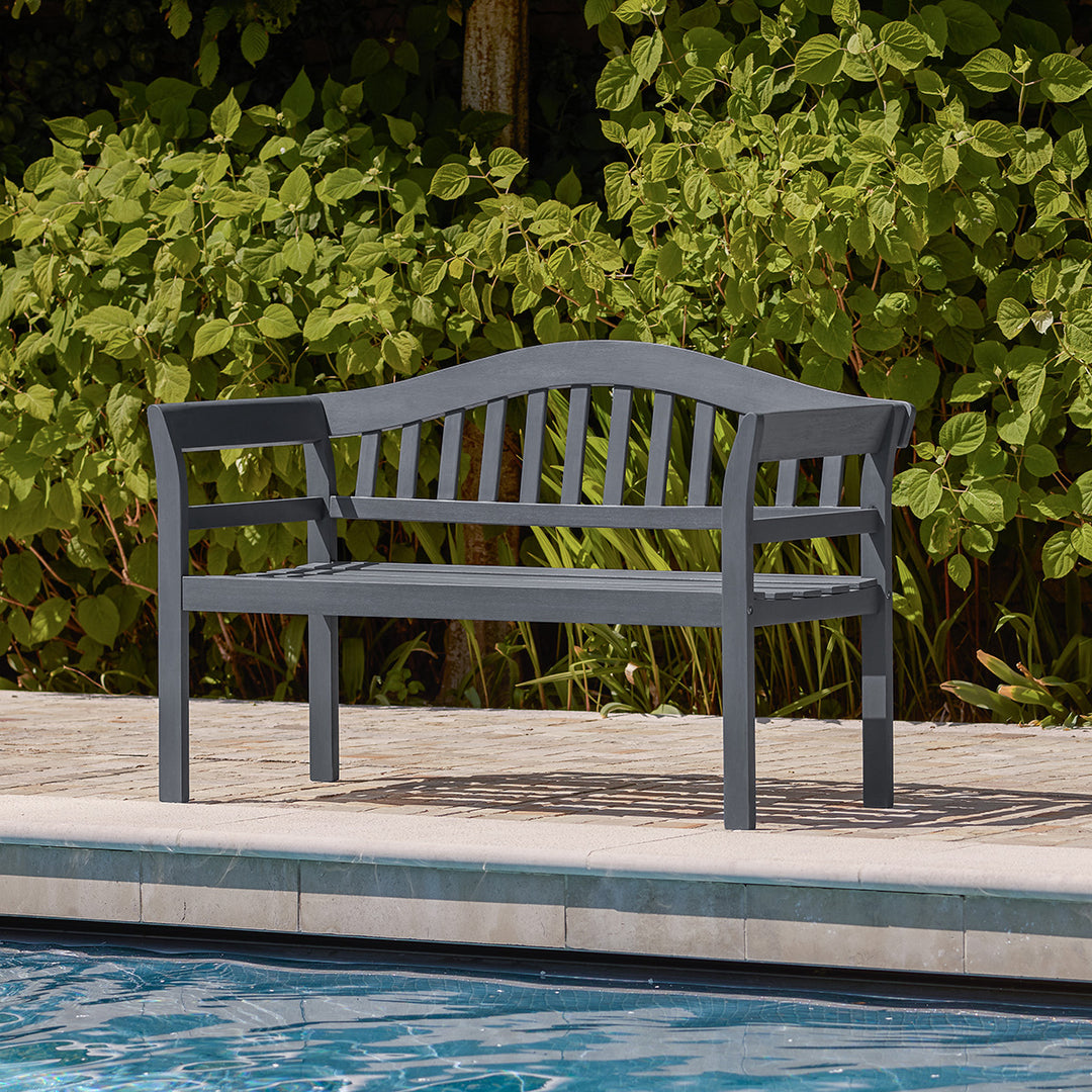 Charcoal wooden garden bench positioned beside a pool, featuring arched backrest and slatted seat in a classic silhouette.