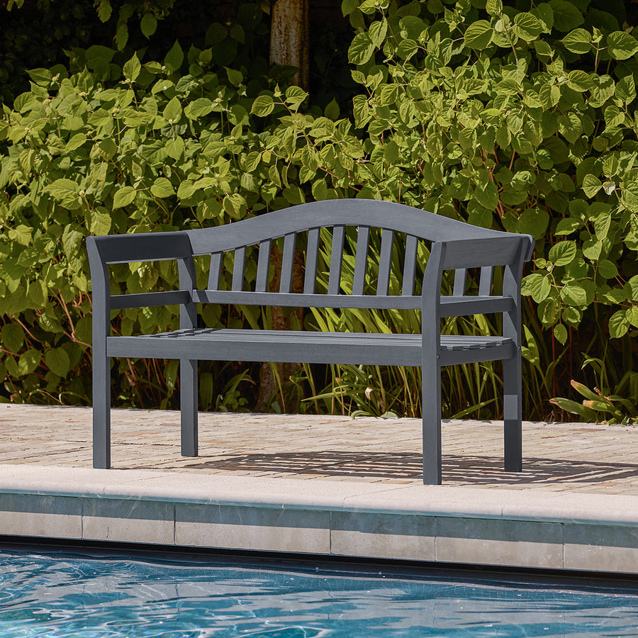 Charcoal wooden garden bench positioned beside a pool, featuring arched backrest and slatted seat in a classic silhouette.