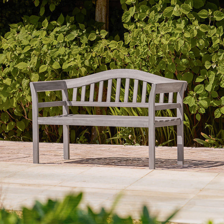 Grey wooden garden bench with traditional curved backrest and arms, styled on a small garden patio.