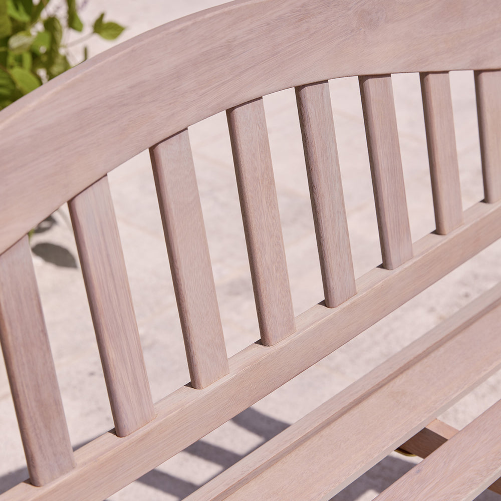 Detail of curved backrest on natural finish wooden garden bench, showing vertical slats and softly sanded grain.
