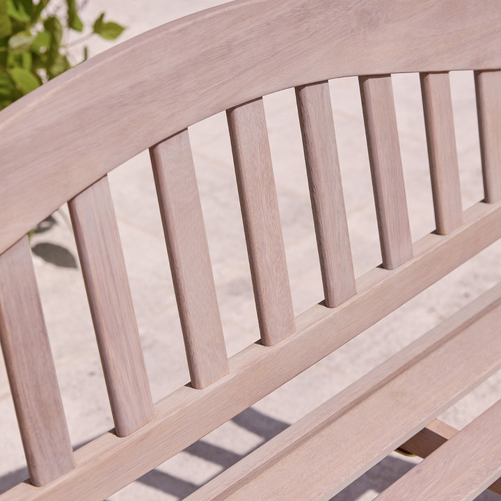 Detail of curved backrest on natural finish wooden garden bench, showing vertical slats and softly sanded grain.