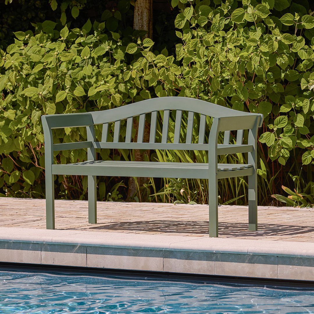 Green wooden garden bench styled poolside with slatted seat and curved back.