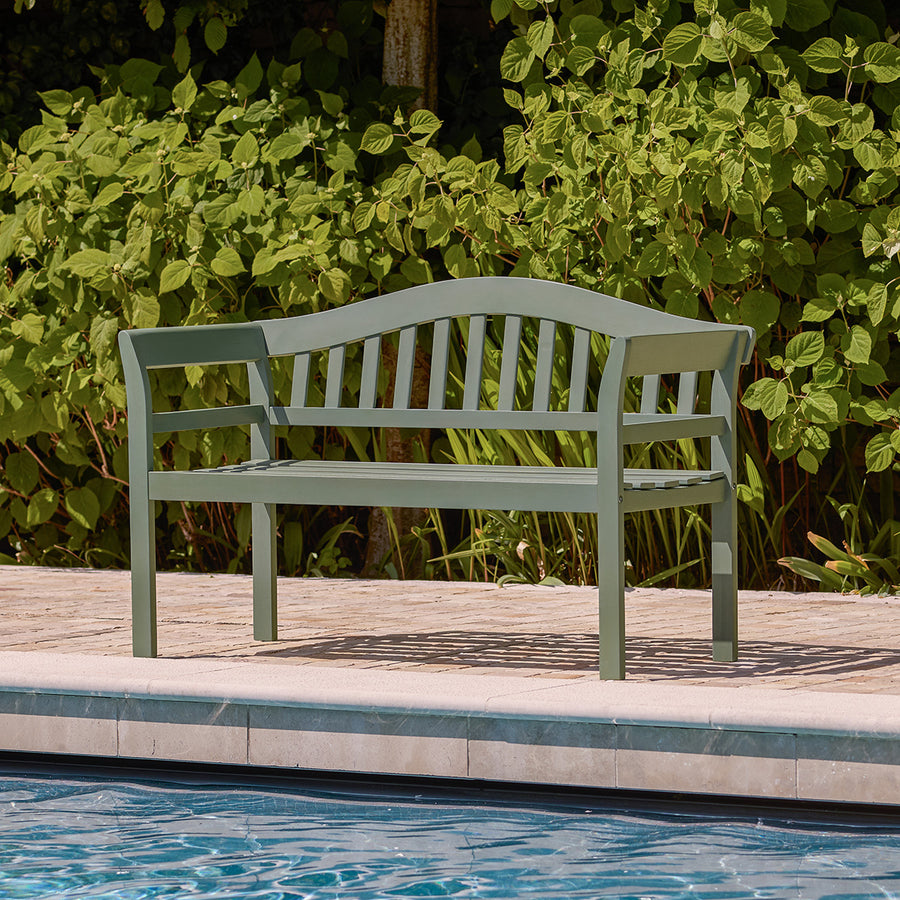 Green wooden garden bench styled poolside with slatted seat and curved back.