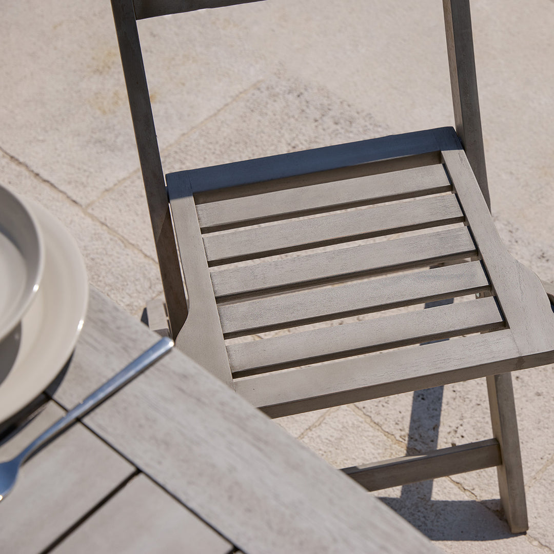 Detail of slatted wooden dining chair from the Repton garden set in light grey finish on a stone terrace.