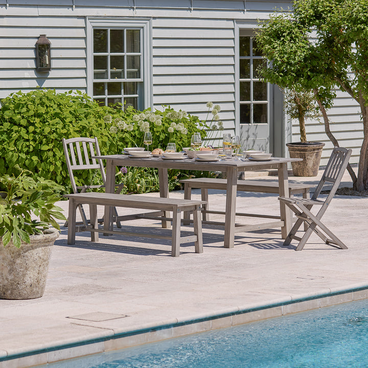 Full Repton wooden garden dining set with bench and chairs styled outdoors on a sunlit patio beside a pool.