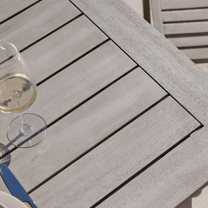 Slatted table top from Repton wooden garden dining set styled with a wine glass and plate on a patio.