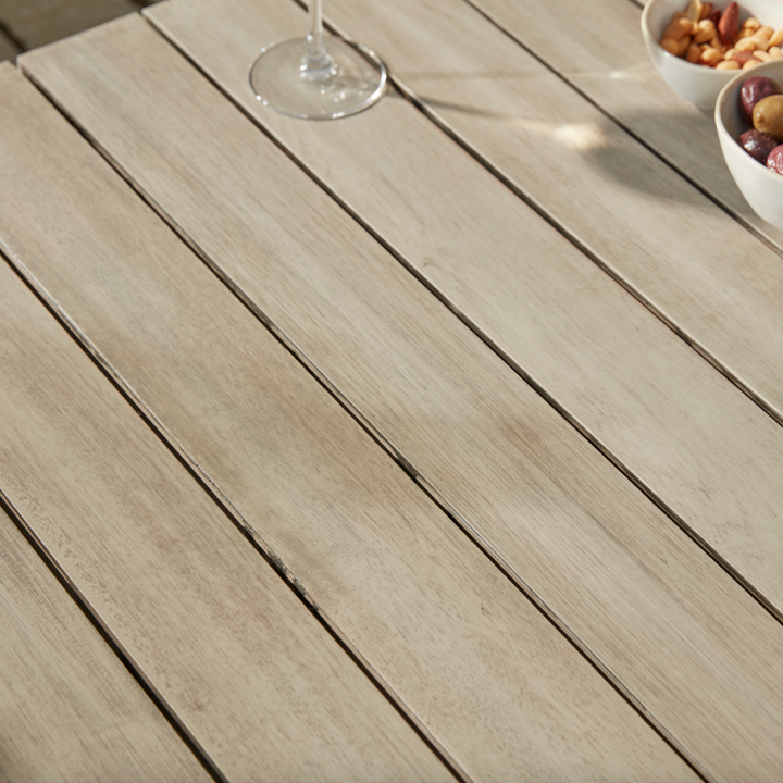 Close-up of the Repton Classic Wooden Garden Coffee Table, highlighting its slatted eucalyptus wood surface with a weathered finish. Styled with a glass of white wine and bowls of nuts and olives, this durable outdoor table is perfect for patios, garden seating, and alfresco dining.