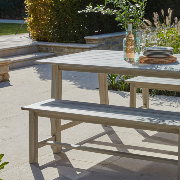 Close up detail of the Repton wooden picnic bench furniture set, on a garden patio and dressed with dinner plates, wine and wine glasses.