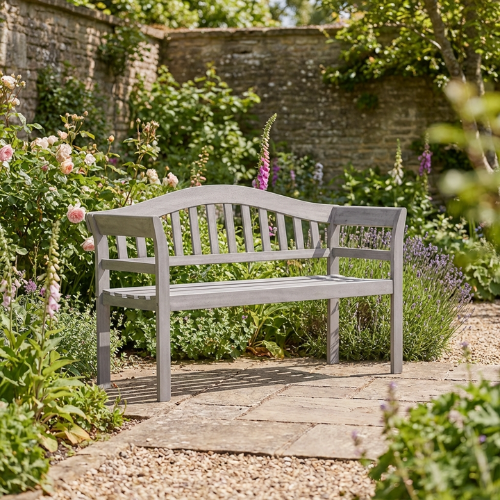 Gray garden bench in a lush cotswold garden setting with cottage garden flowers and a stone wall.
