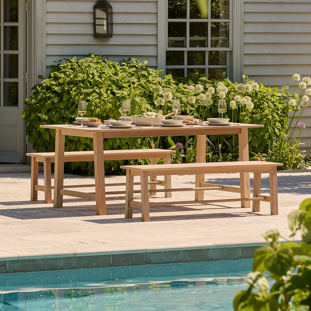 Wooden outdoor dining table with benches by a poolside