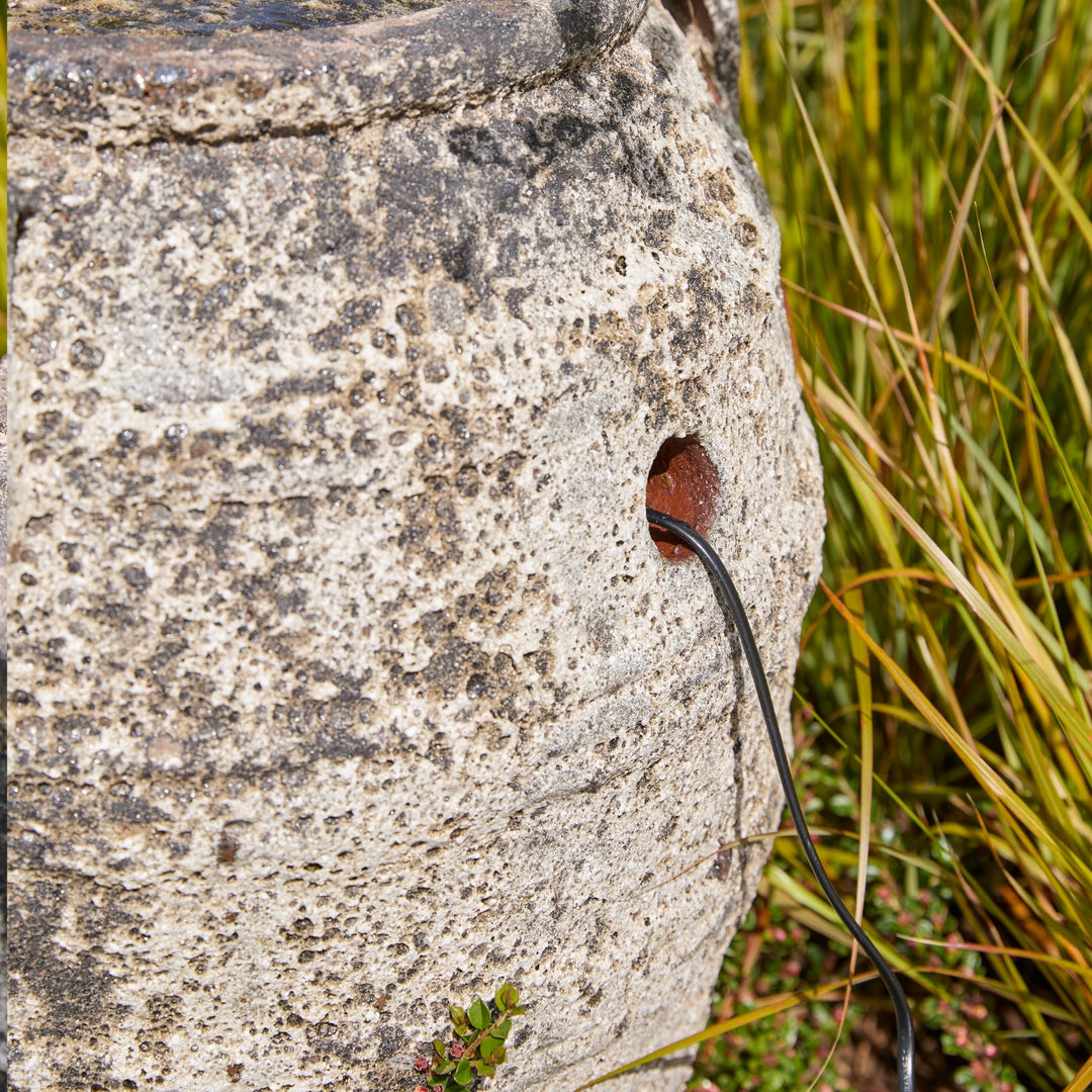 Cable plugged into a stone water feature with grass in the background