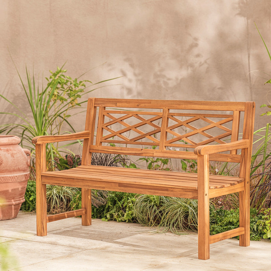 Wooden garden bench with lattice backrest on a wooden deck with plants in the background