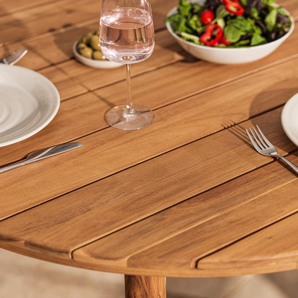 Wooden outdoor table with a glass of water, fork, knife, and salad.