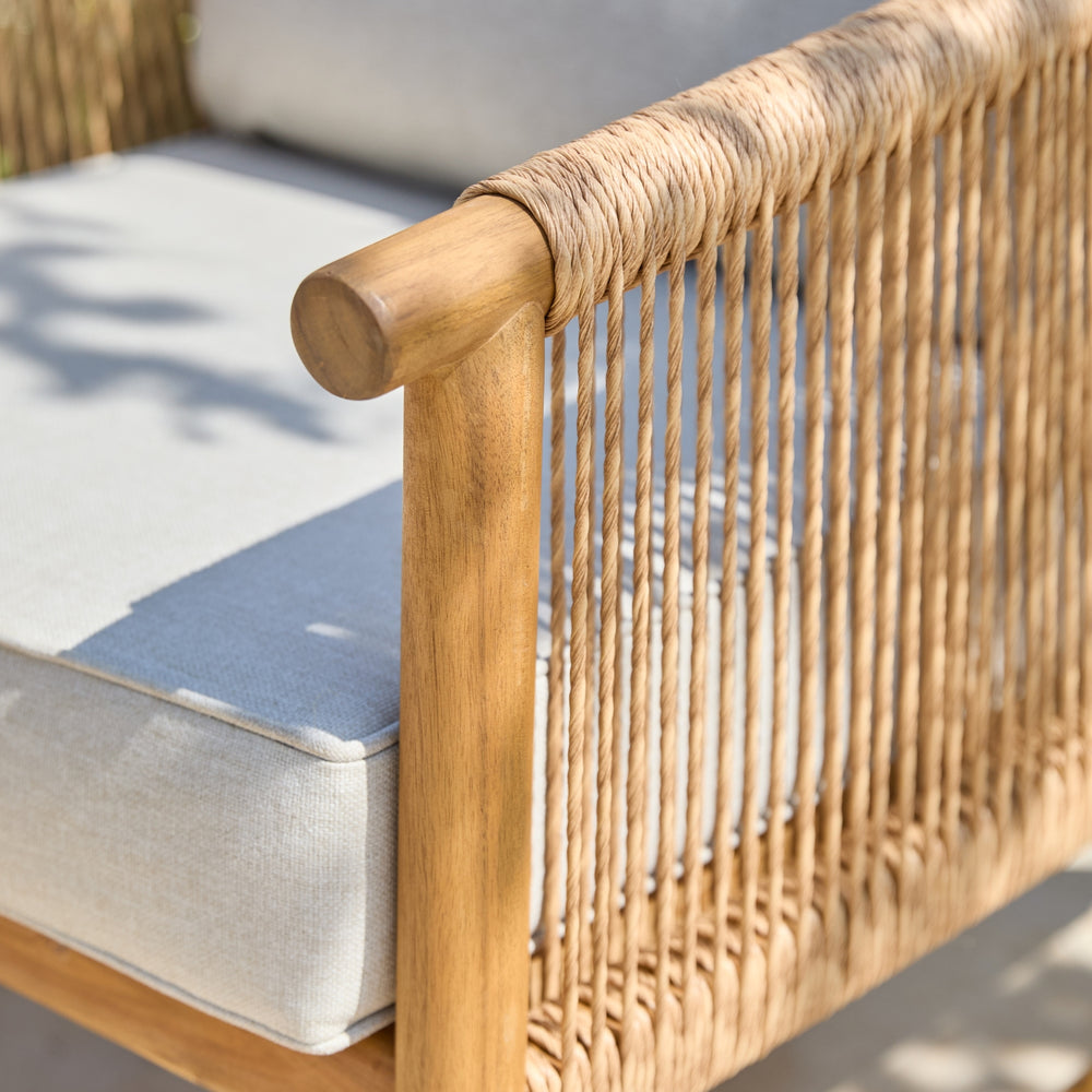 Close-up of a woven rattan or wicker chair frame with a light acacia wood armrest and pale gray cushion.