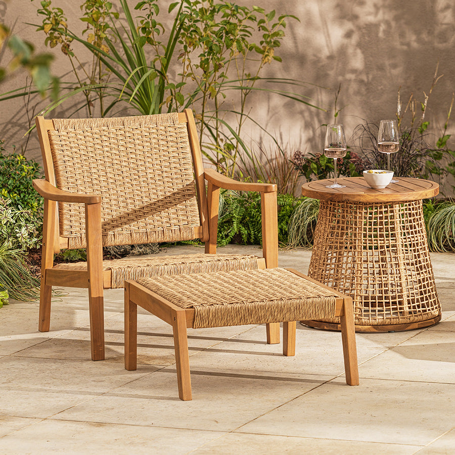 Wicker outdoor furniture set with a chair, ottoman, and table on a patio.