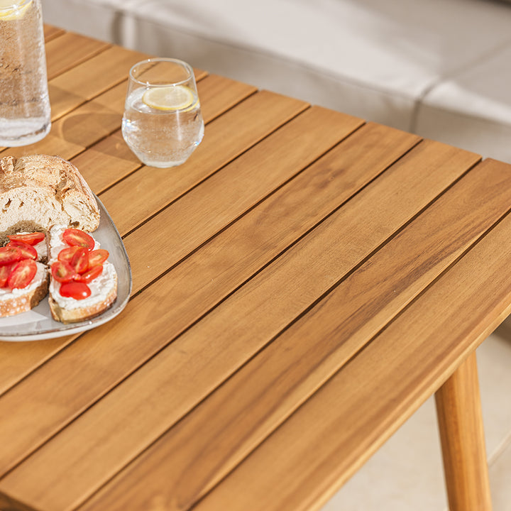Wooden table with a plate of sandwiches and glasses of water on a patio setting