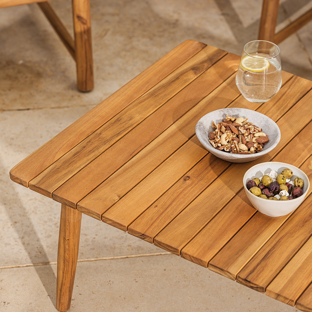 Wooden outdoor table with bowls of snacks and a glass on a stone patio