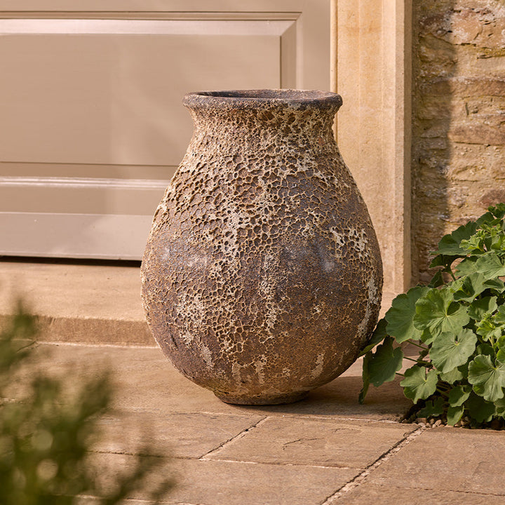 Decorative stone garden urn planter on a patio next to a door and wall.