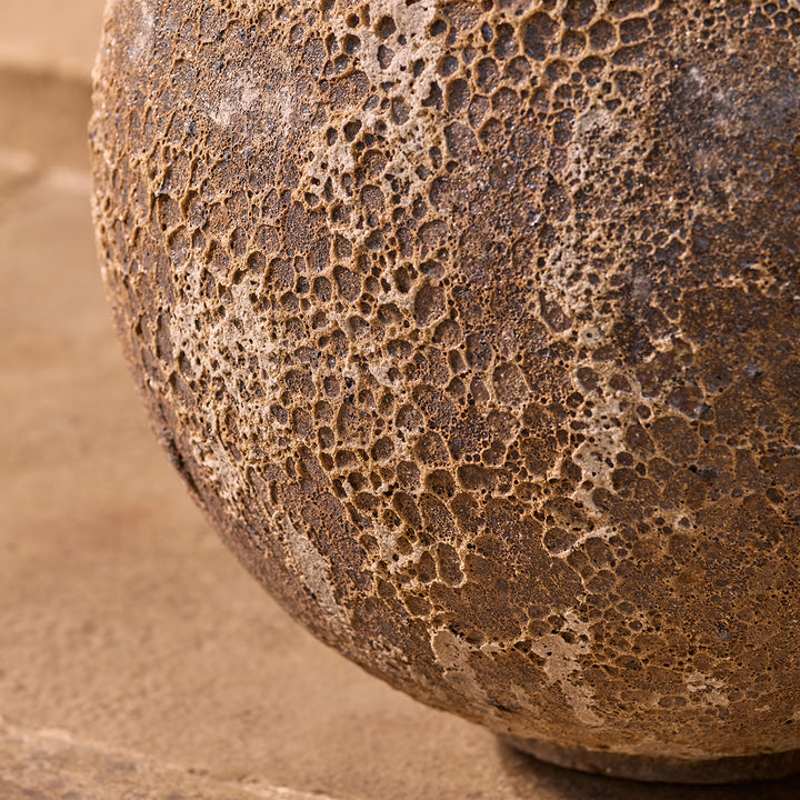 Close-up of a textured stone urn planter on a garden patio background