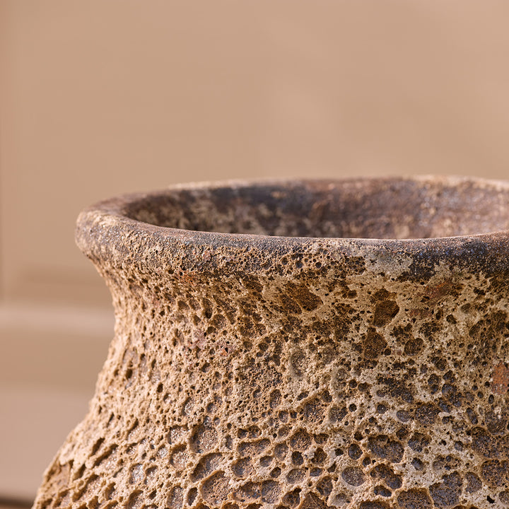Close-up of a textured ceramic urn with a blurred garden background