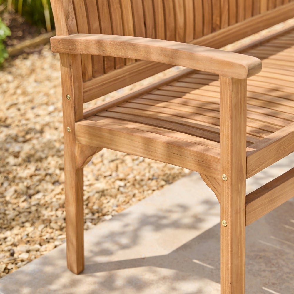 Close-up of a wooden outdoor bench with a slatted seat and curved armrests, shown on a patio beside gravel.