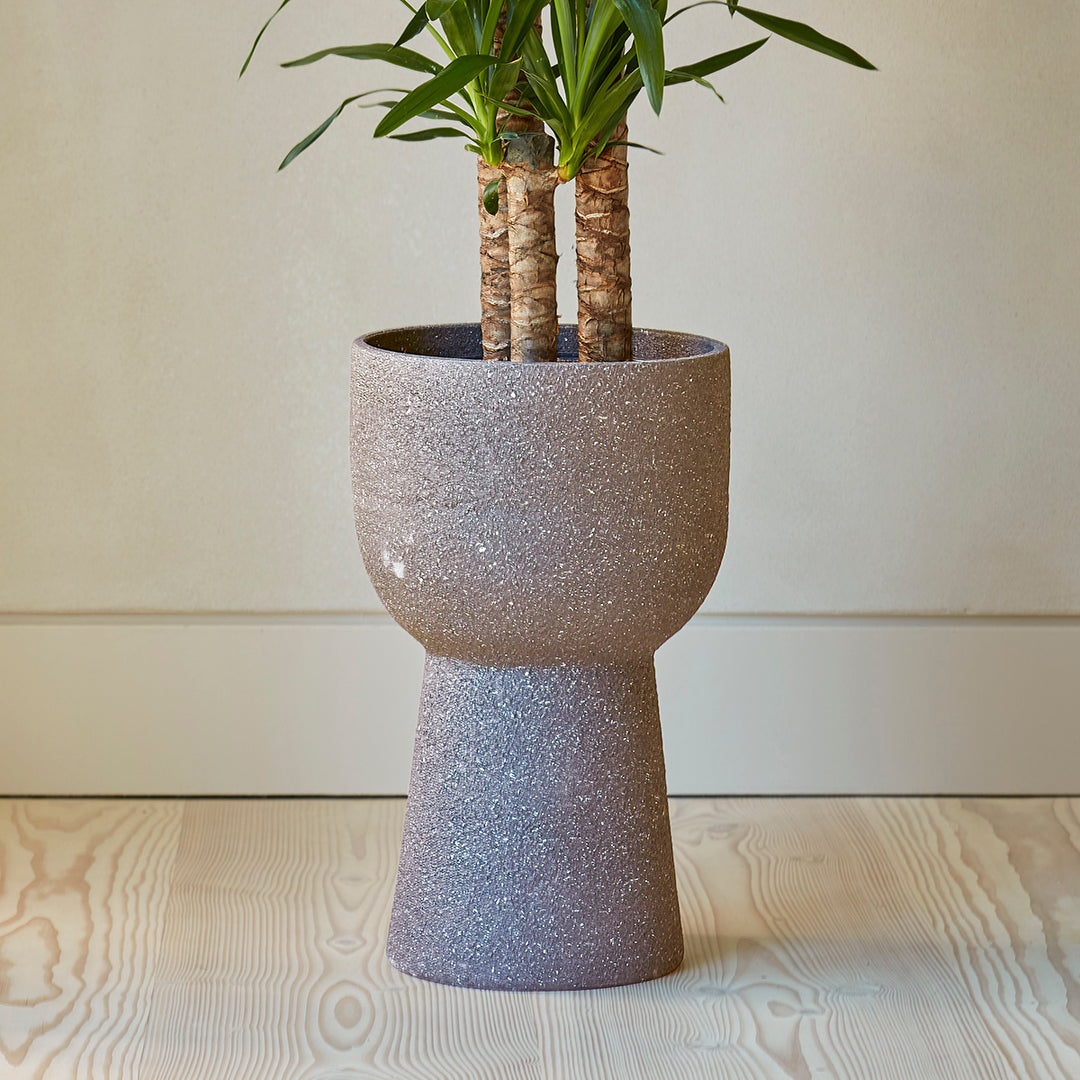Contemporary large grey planter on a stand planted with a yucca tree and placed on on a wooden floor.