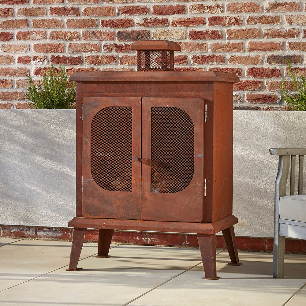 A rustic garden fireplace with it's doors shut next to a cosy seat in a cotswold courtyard garden. The mesh doors show logs stacked inside, ready for the sun to set 