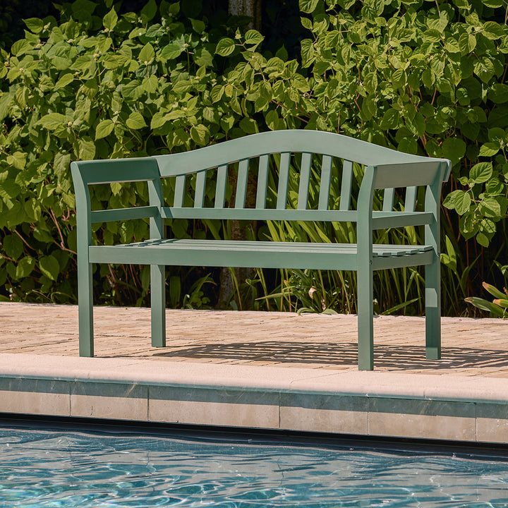 Green painted 2 seater bench styled with a striped towel by a poolside, perfect for relaxed outdoor living.