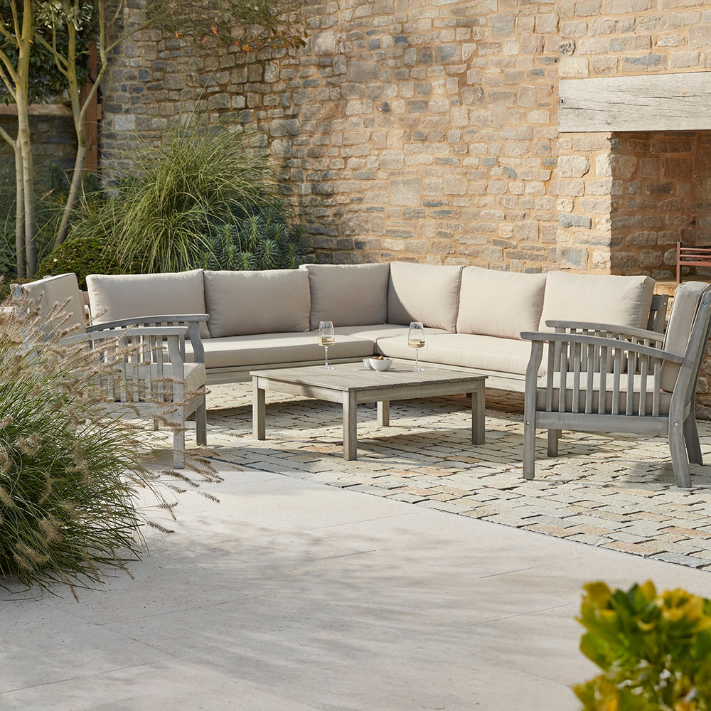 Outdoor patio set with a corner sofa and two wooden armchairs chairs on a stone patio.