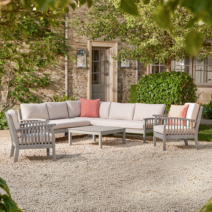 Outdoor patio set with a corner sofa and two wooden armchairs chairs on a stone patio.