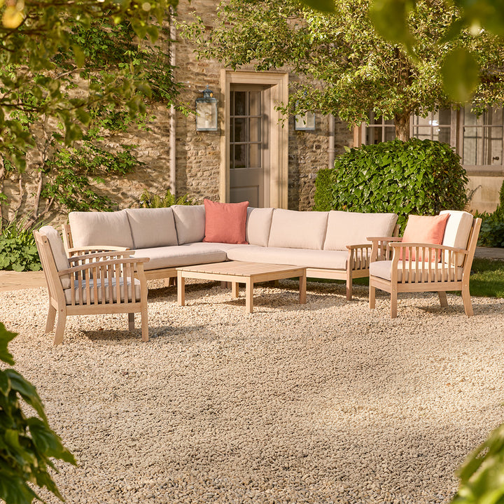 Outdoor patio set with a corner sofa and two wooden armchairs chairs on a gravel patio.