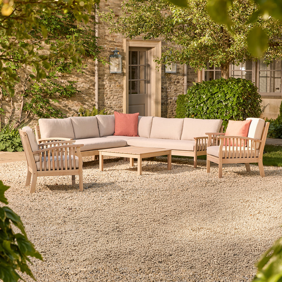 Outdoor patio set with a corner sofa and two wooden armchairs chairs on a gravel patio.