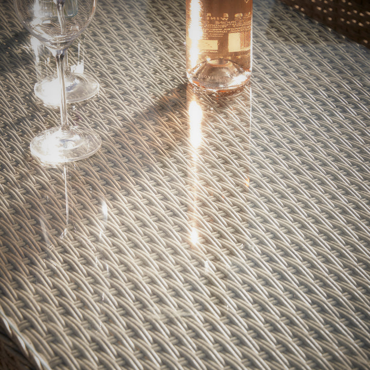 Paxton rattan coffee table with textured woven detail, featuring a glass tabletop with champagne flutes reflecting the sunlight.