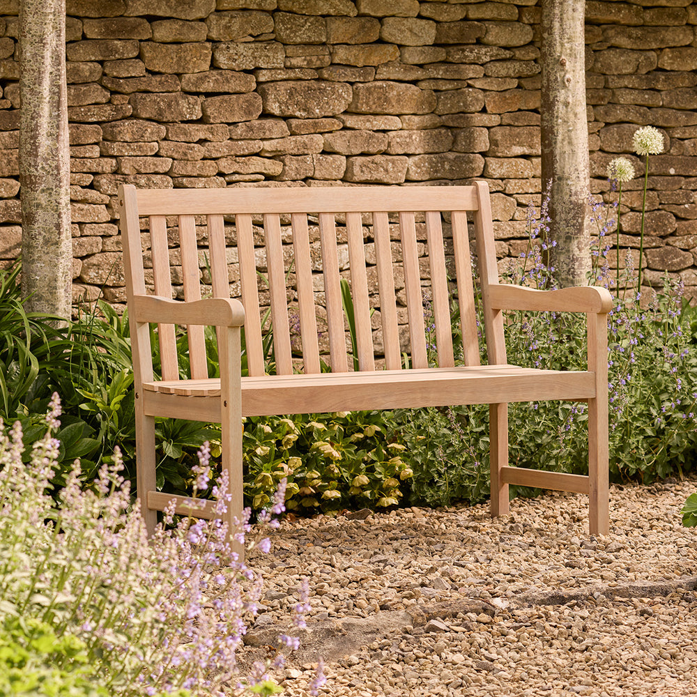 Wooden bench in a garden setting with a stone wall background