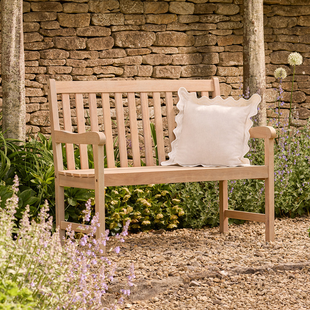 Wooden bench with a white pillow against a stone wall in a garden setting