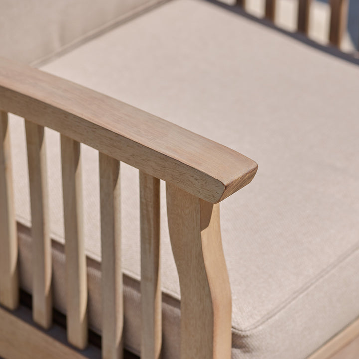 Close-up of curved wooden armrest on outdoor armchair with oatmeal cushion in soft woven fabric.