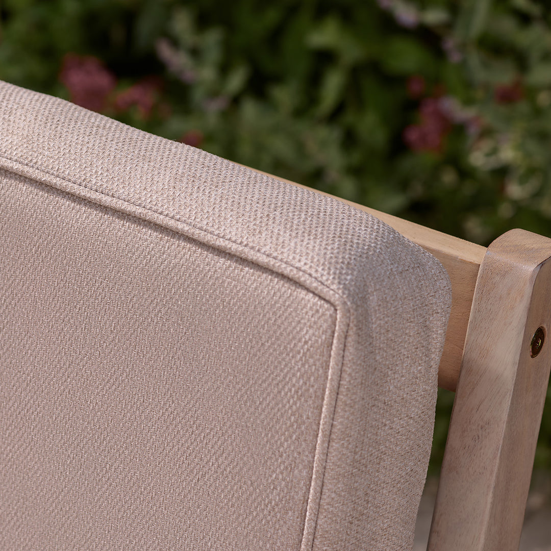 Close-up of oatmeal cushion backrest on wooden outdoor armchair, showing textured fabric and piped edge.