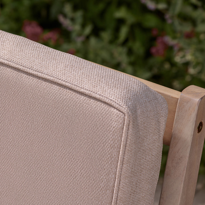 Close-up of oatmeal cushion backrest on wooden outdoor armchair, showing textured fabric and piped edge.