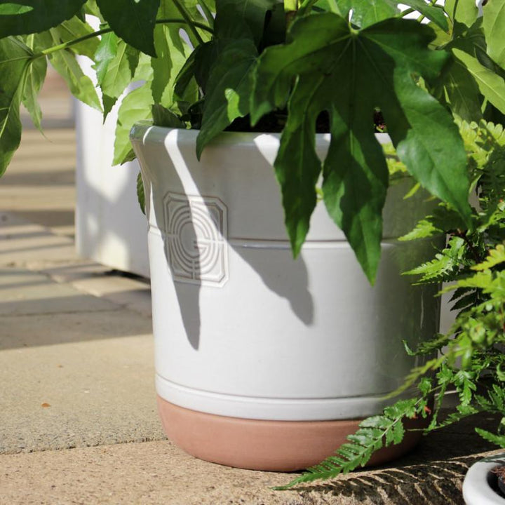 A large white smoke planter partially shaded by tropical foliage, blending seamlessly into a lush garden setting.